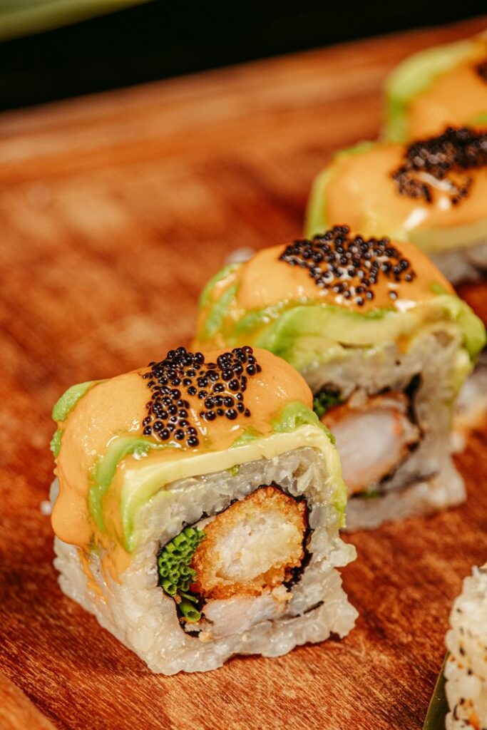 Close-up of sushi rolls topped with avocado and black caviar on a wooden board, perfect for Asian cuisine lovers.